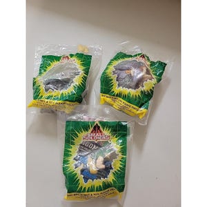 May include: Three sealed Small Soldiers action figures in plastic packaging. The packaging is green with yellow accents and features the Small Soldiers logo. The text "THIS BAG IS NOT A TOY, PLEASE DISCARD" is printed on the packaging.