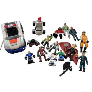 May include: A selection of toy figures and vehicles. Features a silver and blue toy car, a small white vehicle with a red aerial, and various action figures in different outfits. Some figures hold weapons.