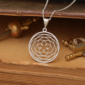May include: A silver necklace with a circular pendant featuring a geometric design of overlapping circles and a flower-like shape in the center.