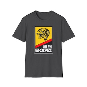 Puede incluir: Camiseta gris oscuro con un diseño gráfico rectangular. El diseño presenta una cabeza de tigre en negro y amarillo, con texto rojo y blanco en un idioma extranjero. La camiseta está hecha de un material suave.