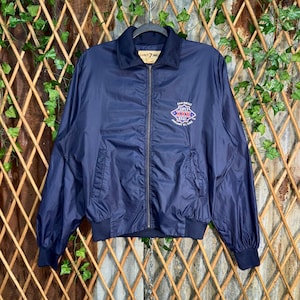 Può includere: Giacca blu navy con zip e colletto e polsini blu scuro. La giacca presenta un logo del Super Bowl XXIII di San Diego sul petto. Ha due tasche anteriori e una chiusura con zip completa.