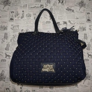 以下が含まれることがあります： ネイビーブルーのキルティングトートバッグ。ダイヤモンド模様と小さなゴールドスタッズが特徴。黒いハンドルと装飾的なエンブレムが付いています。スタイリッシュで機能的なアクセサリーです。