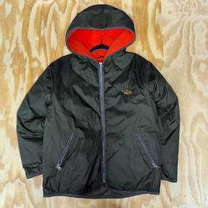 May include: A reversible hooded jacket in dark green with a bright orange interior. The jacket has a full zipper, two front pockets, and a small embroidered design on the chest. The hood is lined with orange fleece.