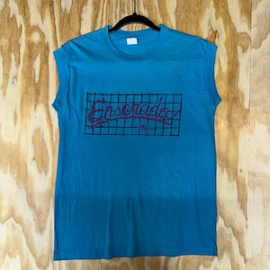 May include: A sleeveless turquoise t-shirt with the word "Ensenada" in a pink script font, set against a black grid. The word "Mexico" is below the main text. The shirt is hanging on a black hanger.