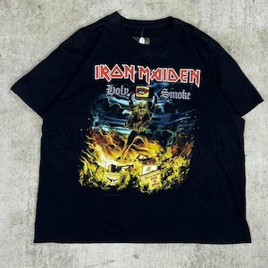 Könnte beinhalten: Schwarzes T-Shirt mit dem Bandnamen "Iron Maiden" in Rot und einer Grafik für den Song "Holy Smoke". Die Grafik zeigt eine Figur, die eine Kiste über Flammen hält. Das T-Shirt hat einen klassischen Rundhalsausschnitt.