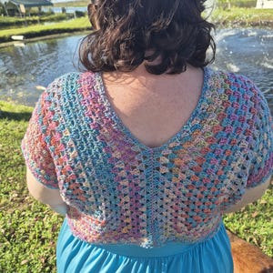 May include: A woman wearing a multi-colored crochet top with a blue v-neck and a blue skirt.
