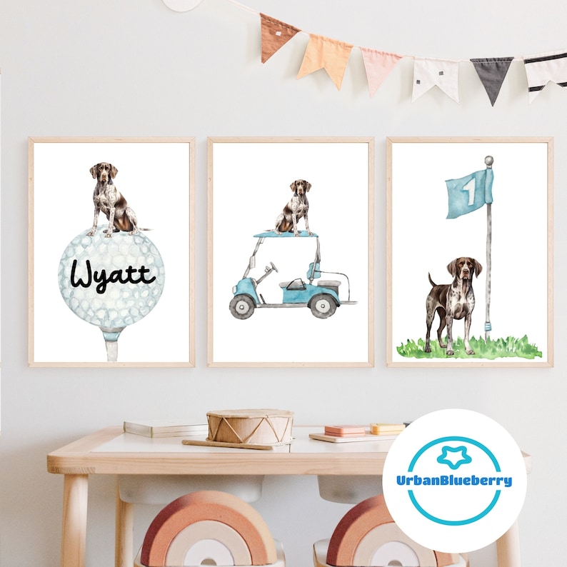 Op de afbeelding: Drie aquarelprints met een bruine en witte hond. De eerste print toont de hond zittend op een golfbal met de naam Wyatt erop. De tweede print toont de hond zittend in een blauwe golfkar. De derde print toont de hond staand op een groene grasstrook met een blauwe vlag met het nummer 1 erop.