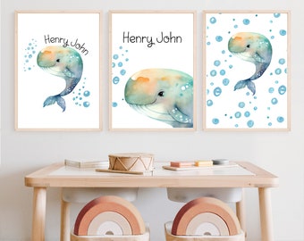 May include: Three framed watercolor prints featuring a whale illustration in shades of blue, teal, and orange. Each print has the name "Henry John" in black script. The prints are displayed above a small wooden table with two rainbow-shaped stools.