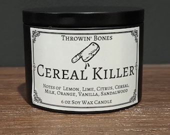 May include: Black candle jar with a white label that reads "THROWIN' BONES CEREAL KILLER" with a drawing of a butcher knife. The label also lists the scent notes: "NOTES OF LEMON, LIME, CITRUS, CEREAL, MILK, ORANGE, VANILLA, SANDALWOOD" and "6 OZ SOY WAX CANDLE".