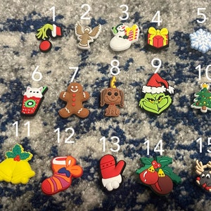 Peut inclure: Un ensemble de 15 breloques de chaussures sur le thème de Noël, représentant divers icônes des fêtes comme un bonhomme de neige, un bonhomme en pain d'épices, un sapin de Noël et le Grinch. Les breloques sont en caoutchouc coloré et sont numérotées de 1 à 15.