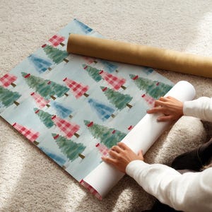 May include: Wrapping paper featuring a repeating pattern of Christmas trees in red, green, and blue on a light blue background. A brown cardboard tube and a white paper roll are also visible.