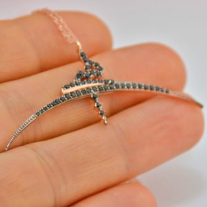 May include: A delicate necklace with a curved, abstract design set with black diamonds. The necklace is made of rose gold and features a delicate chain.
