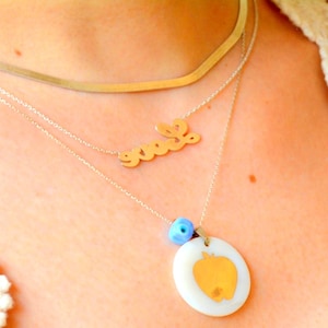 May include: A layered necklace set. It includes a gold-toned choker, a chain with the word "love", and a pendant necklace with an oval pendant and an apple design. The pendant has a blue bead above it.