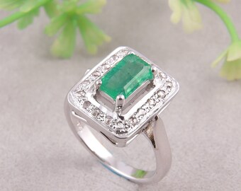 May include: A silver ring with a large emerald green gemstone surrounded by a halo of smaller diamonds.