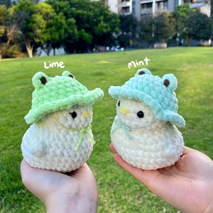 May include: Two white crocheted plush toys wearing green frog hats. The hat on the left is lime green and the hat on the right is mint green. The text "Lime" is above the left toy and the text "Mint" is above the right toy.