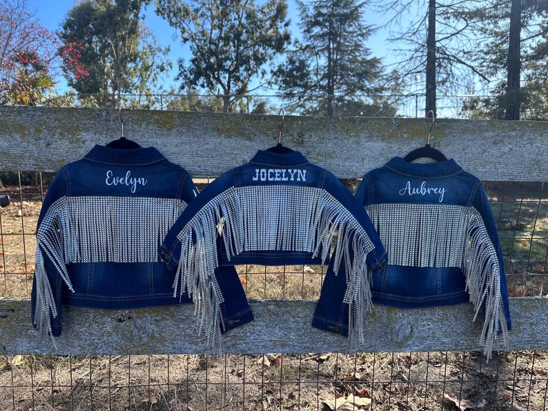 Puede incluir: Tres chaquetas vaqueras con pedrer&iacute;a y flecos. Las chaquetas est&aacute;n personalizadas con los nombres "Evelyn", "Jocelyn" y "Aubrey".