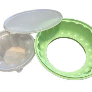 May include: Three plastic molds for making gelatin desserts. One is light green, the other is clear with a lid, and the third is clear with a lid. The green mold has a ring shape with a scalloped edge. The clear molds have a rounded shape.