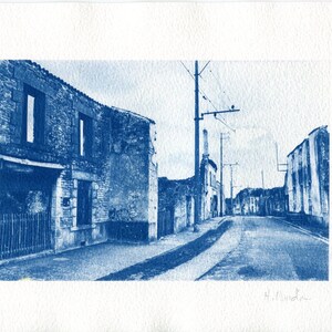 Puede incluir: Una fotografía cianotipo en tonos azules, que representa una calle en un pueblo pequeño. La calle está bordeada de edificios antiguos de piedra con ventanas y puertas. Los edificios parecen estar en estado de deterioro. La calle está vacía y el cielo está nublado.