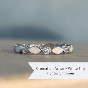 May include: A white gold band ring with small diamonds and white cremation ashes embedded in the band. The text on the image reads "Cremation Ashes + White Tint + Snow Shimmer".