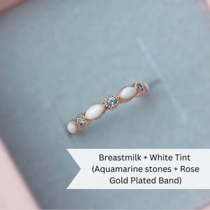 May include: A delicate ring made with breastmilk and white tint, featuring aquamarine stones and a rose gold plated band.