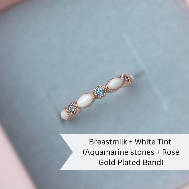 May include: A delicate ring made with breastmilk and white tint, featuring aquamarine stones and a rose gold plated band.