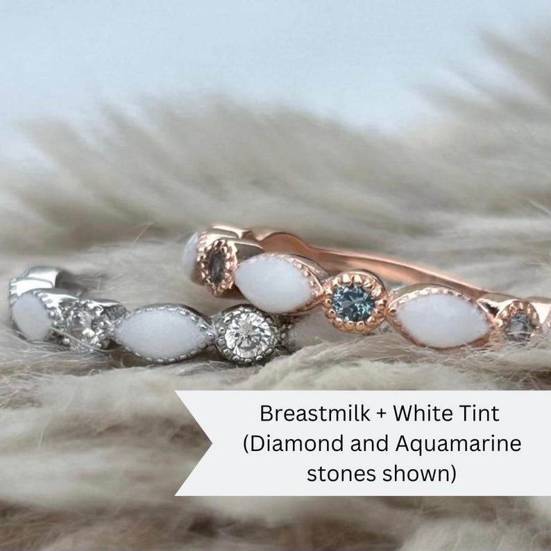 May include: Two delicate rings with white oval stones and small accent stones. The top ring has aquamarine accent stones and is set in rose gold. The bottom ring has diamond accent stones and is set in silver. The text "Breastmilk + White Tint (Diamond and Aquamarine stones shown)" is below the rings.