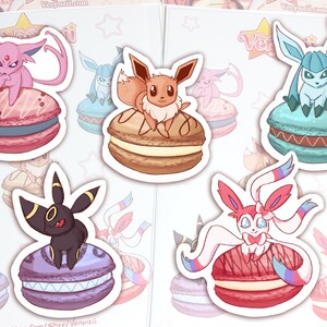 May include: Five colorful macaron stickers featuring different Pokemon characters. Each sticker has a Pokemon character sitting on top of a macaron. The macarons are pink, brown, blue, purple, and red.