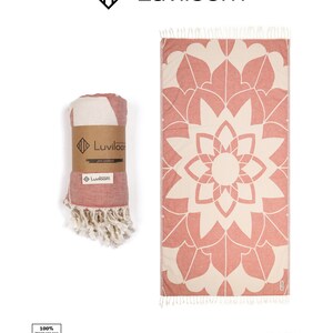 May include: A rectangular Turkish cotton towel featuring a terracotta and cream mandala pattern with tasseled ends. One towel is rolled and secured with a brown paper band labeled Luviloom, while the other is displayed flat to show the full design.