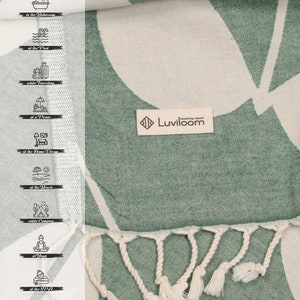 May include: A sage green and off-white woven textile featuring a large leaf pattern, a cream-colored brand label reading Luviloom, and knotted fringe trim. A vertical sidebar displays icons for bathroom, pool, travel, picnic, home decor, beach, camping, yoga, spa, and gym use.