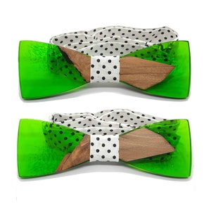 Può includere: Un papillon verde e legno con un motivo a pois bianchi e neri. Il papillon è composto da due pezzi di acrilico verde e un pezzo di legno.