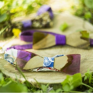 Può includere: Papillon in legno con dettagli viola e dettagli in tessuto fantasia sono esposti su una superficie di legno. I papillon hanno un aspetto naturale venato e sono circondati dal verde.