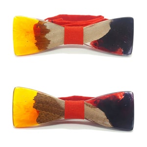 Può includere: Due papillon in legno con dettagli in resina rossa, gialla, marrone e nera. I papillon hanno un cinturino in tessuto rosso.