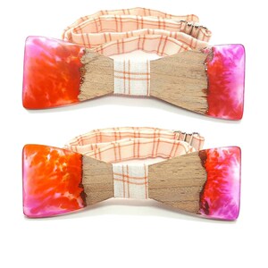 Può includere: Due papillon in legno con un design in resina rosa e arancione. I papillon hanno un cinturino regolabile a quadri bianchi e arancioni.