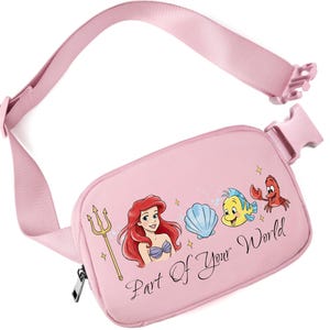 May include: Pink fanny pack featuring Ariel from The Little Mermaid, a seashell, Flounder, and Sebastian. The text "Part Of Your World" is printed on the front. The adjustable strap and buckle are also pink.