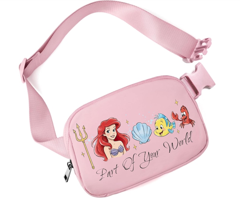 May include: Pink fanny pack featuring Ariel from The Little Mermaid, a seashell, Flounder, and Sebastian. The text "Part Of Your World" is printed on the front. The adjustable strap and buckle are also pink.