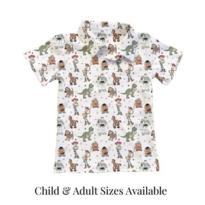 May include: White short-sleeved collared shirt with a repeating pattern of cartoon characters. The shirt features characters like a dinosaur, a cowboy, and a space ranger. The text "Child & Adult Sizes Available" is at the bottom.