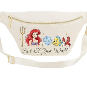 May include: Cream-coloured fanny pack with a gold zip and buckle. The front features a colourful illustration of Ariel, a seashell, Flounder, and Sebastian, with the text "Part of Your World". The adjustable strap is cream-coloured.