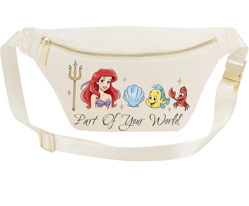 May include: Cream-coloured fanny pack with a gold zip and buckle. The front features a colourful illustration of Ariel, a seashell, Flounder, and Sebastian, with the text "Part of Your World". The adjustable strap is cream-coloured.
