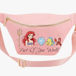 May include: Pink fanny pack with a gold zip and buckle. The pack features a graphic of Ariel, Flounder, Sebastian, and a seashell, with the text "Part of Your World". The adjustable strap is also pink.