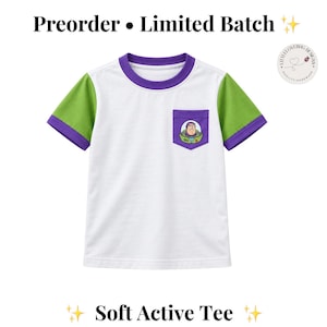 May include: A white short-sleeve t-shirt with a purple crew neckline and green sleeves. The shirt features a purple chest pocket with a graphic of a space ranger character. Text at the top reads Preorder Limited Batch and Soft Active Tee.