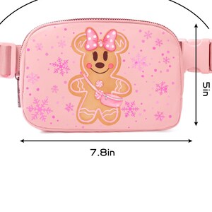 May include: Pink fanny pack with a gingerbread man design. The bag is 7.8 inches wide and 5 inches tall, with an adjustable strap that fits waists from 28 to 44 inches. The gingerbread man has a pink bow and a small pink purse.