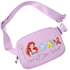 May include: A lilac fanny pack with a matching adjustable strap and buckle. The pack features a graphic of Ariel, Flounder, Sebastian, and a seashell. The text "Part Of Your World" is printed on the front.