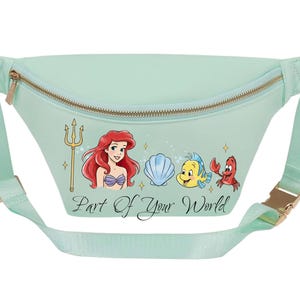 May include: A mint green fanny pack with a gold zip and buckle. The front features a graphic of Ariel, Flounder, Sebastian, and a seashell, with the text "Part of Your World". The adjustable strap matches the bag's colour.
