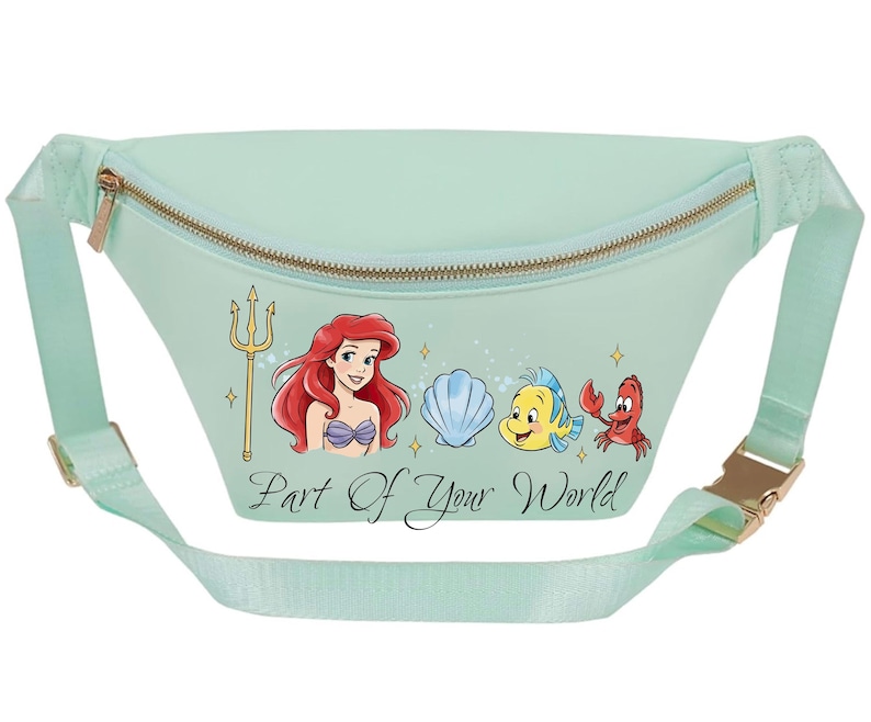 May include: A mint green fanny pack with a gold zip and buckle. The front features a graphic of Ariel, Flounder, Sebastian, and a seashell, with the text "Part of Your World". The adjustable strap matches the bag's colour.