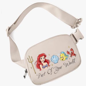 May include: Beige fanny pack with a colourful illustration of Ariel and friends from The Little Mermaid. The text "Part Of Your World" is written in a script font. The adjustable strap and buckle are beige.
