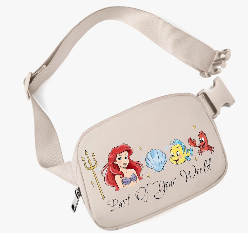 May include: Beige fanny pack with a colourful illustration of Ariel and friends from The Little Mermaid. The text "Part Of Your World" is written in a script font. The adjustable strap and buckle are beige.