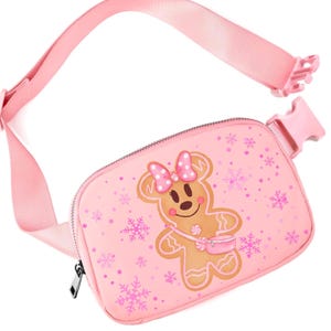 May include: Pink fanny pack with a gingerbread person design. The bag features a pink strap and buckle, a zipper closure, and a repeating snowflake pattern. The gingerbread person has a pink bow and a small purse.