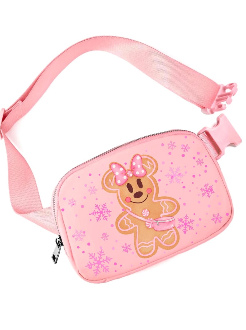 May include: Pink fanny pack with a gingerbread person design. The bag features a pink strap and buckle, a zipper closure, and a repeating snowflake pattern. The gingerbread person has a pink bow and a small purse.