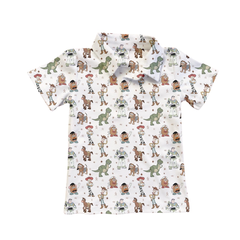 May include: White short-sleeved polo shirt with a repeating pattern of Toy Story characters. The design includes images of Woody, Buzz Lightyear, Rex, Mr. Potato Head, and other characters from the animated film. The shirt has a collared neckline.