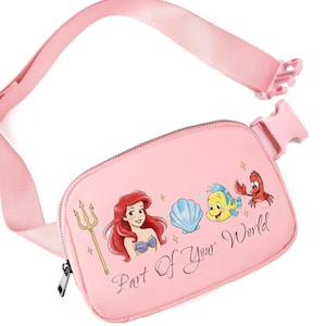 May include: Pink fanny pack with a graphic of Ariel, Flounder, Sebastian, and a seashell. The text "Part Of Your World" is printed on the front. It has a zip closure and an adjustable strap.